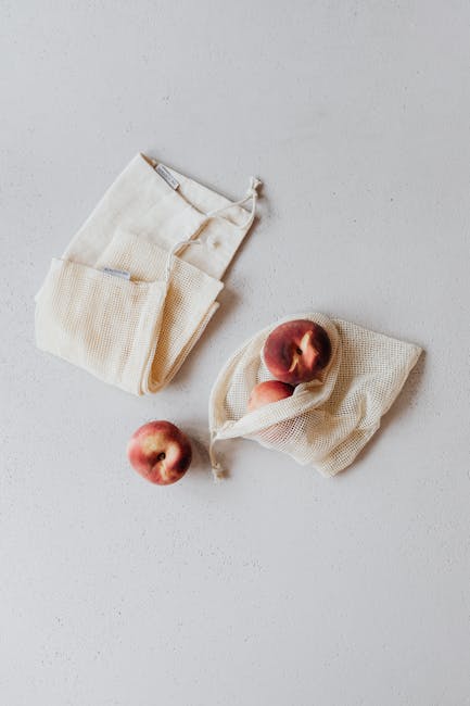 Top view of eco-friendly mesh bags containing fresh peaches on a white surface.